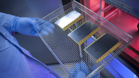 Gloved hands wearing a metal tray with three semiconductor components prepared for extreme temperature testing