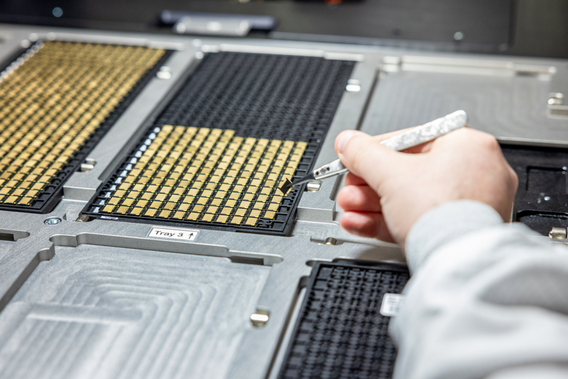 Hand manipulating microchips with tweezers on a wire mesh tray in a laboratory environment