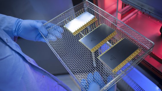 Gloved hands wearing a metal tray with three semiconductor components prepared for extreme temperature testing