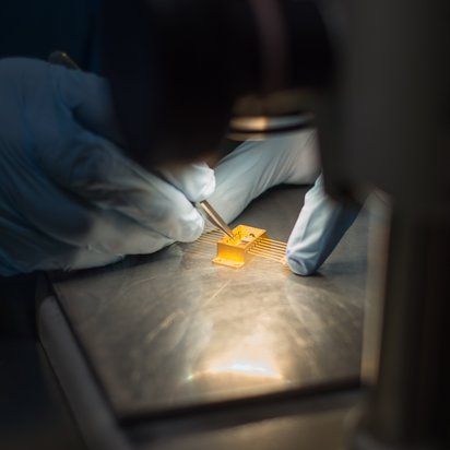 Technician working with a small photonic butterfly device under a microscope.